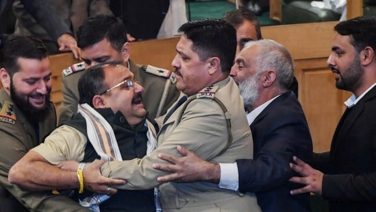 Srinagar, Nov 07 (ANI): Marshals remove BJP MLA after a brawl breaks out over a banner on the restoration of Article 370 displayed by Awami Ittehad Party (AIP) MLA and brother of Lok Sabha MP Engineer Rashid, Khurshid Ahmad Sheikh in the Jammu and Kashmir Legislative Assembly session, in Srinagar on Thursday. (ANI Photo) 