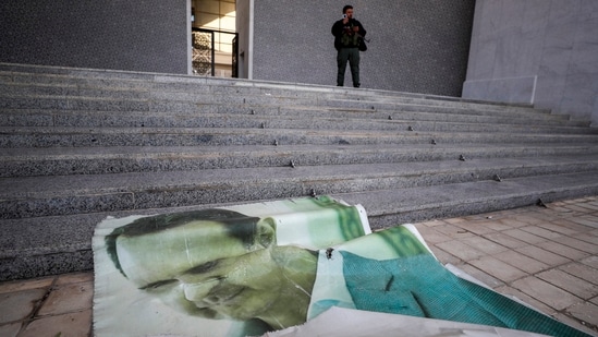 A giant picture of Syrian President Bashar Assad lies on the ground as a Syrian opposition fighter stands nearby, inside the Presidential Palace in Damascus, Syria, Sunday, Dec. 8, 2024. AP/PTI(AP12_08_2024_000124B)(AP)