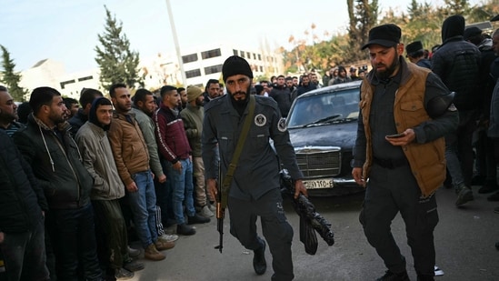 Members of Syria's new authorities walk followed by a car as Syrian soldiers, (AFP)