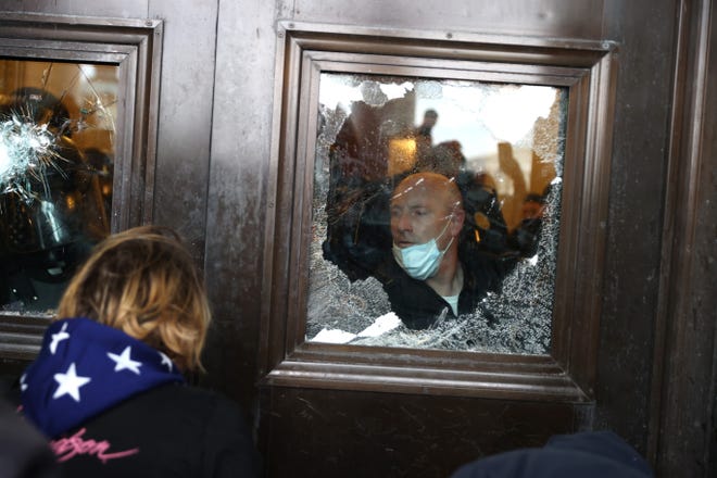 A Capitol police officer looks out of a broken window as rioters gather in the Capitol Building on Jan. 6, 2021 A pro-Trump mob disrupted the official certification of Joe Biden's victory in the 2020 election.