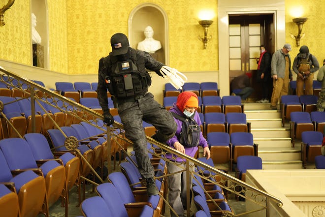 A rioter wearing tactical garb and carrying zip-tie handcuffs clambers across the Senate gallery during the Jan. 6, 2021, assault on the U.S. Capitol by followers of President Donald Trump.